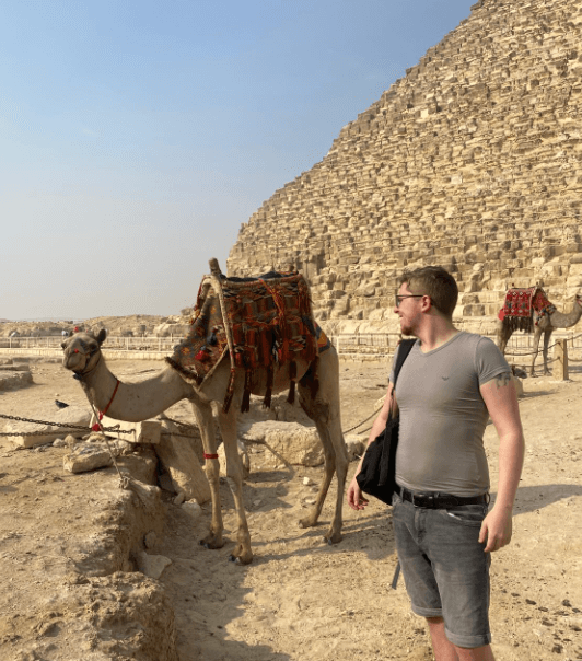 Reisender steht neben einem Kamel an den Pyramiden in Ägypten