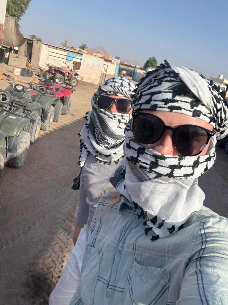 Zwei Reisende mit Tuch und Sonnenbrille stehen vor einer Reihe Quads in der ägyptischen Wüste, bereit für ihre Quad Tour in Hurghada.